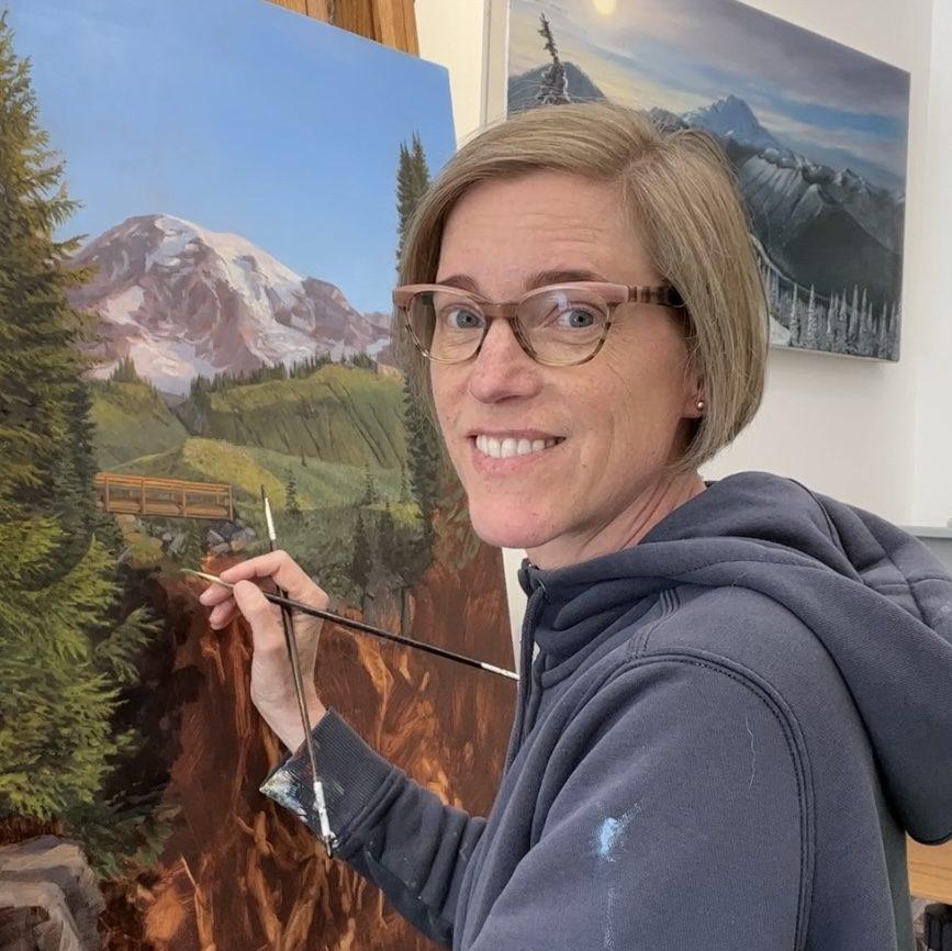 Photo of Mary Iverson painting a mountains, cliffs, and forest landscape on canvas. 